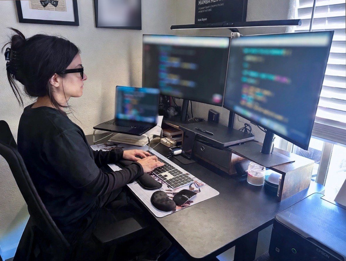 Romi at her desk building an app on two large monitors and a laptop