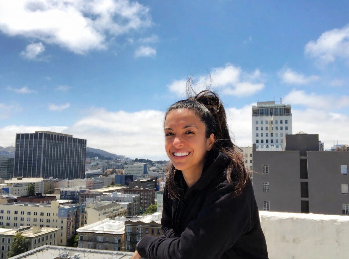 Romi smiling on a rooftop, looking out over the city